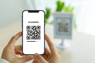 The woman's hand is using the phone to scan the qr code to selec